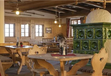 A cozy restaurant with wooden furniture and a green stove. The walls are made of wood, and large windows provide plenty of light.
