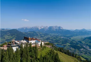 A picturesque mountain landscape with a mountain hut in the foreground. In the background, majestic mountains rise under a clear blue sky.