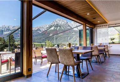 Ein modernes Restaurant mit Holzdekor und Tischen ist zu sehen. Durch große Fenster bietet sich ein spektakulärer Blick auf die Berge.
