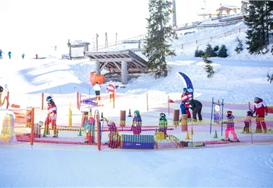 A colorful play area in the snow, where children learn to ski. Surrounded by snow-covered trees and a mountainous landscape.
