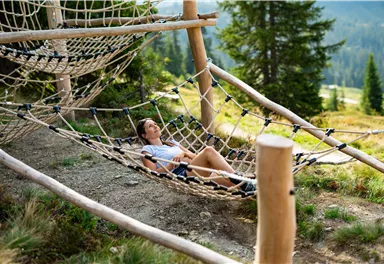 A person relaxes in a hammock in nature. In the background, there are trees and a picturesque landscape.