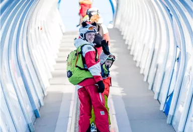 A group of skiers stands in a colorful tunnel that leads to the ski resort. The atmosphere is cheerful and wintry.