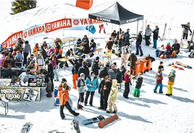 A lively winter event with many people in the snow. Tables and stalls are set up, and the attendees enjoy the atmosphere.