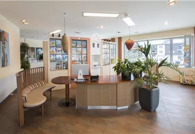 Ein modern eingerichteter Empfangsbereich mit einem runden Tisch und einer Sitzbank. Große Fenster und Pflanzen sorgen für eine freundliche Atmosphäre.