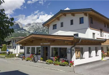 A cozy restaurant with a beautiful wooden porch. In the background, the mountains and a clear blue sky can be seen.
