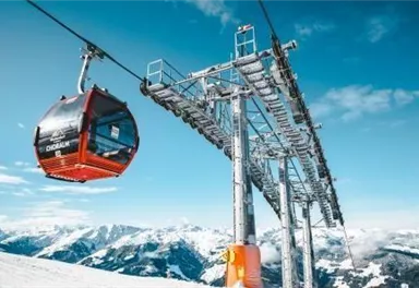 Eine Seilbahn fährt über schneebedeckte Berge. Der Himmel ist klar und blau.