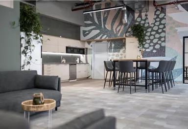 Eine moderne Büroküche mit einem großen Tisch und Stühlen. Die Wände sind mit bunten, floralen Mustern dekoriert.