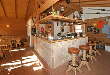 A cozy bar with wooden decor and a stone background. Bright rays of light stream through the windows, creating an inviting atmosphere.