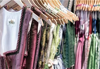 A selection of traditional garments hangs on hangers. The colors range from pink to green, with fine details and embellishments.