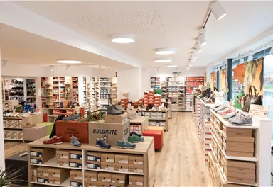 Ein modern gestalteter Schuhladen mit hellen Regalen und einer Vielzahl von Schuhen. Die Beleuchtung sorgt für eine einladende Atmosphäre.