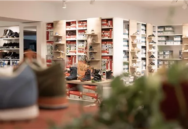 Ein Schuhgeschäft mit Regalen voller Schuhe. Im Vordergrund sind mehrere Schuhpaare sichtbar.