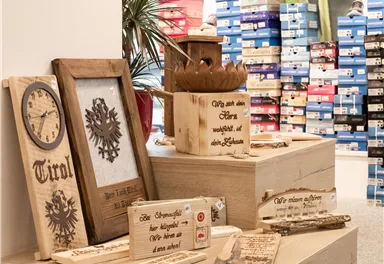 Ein Verkaufsdisplay mit dekorativen Holzobjekten steht im Vordergrund. Im Hintergrund sind Regale mit farbigen Schuhkartons sichtbar.