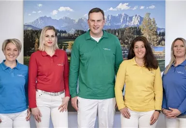 A group of five people stands together, all wearing colorful polo shirts in various colors. In the background, a mountain landscape can be seen.