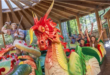 Ein bunter Drachenpark mit fröhlichen Kindern und einem freundlichen Ritter. Die Atmosphäre ist lebhaft und einladend.