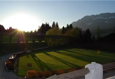 A beautiful landscape with gentle hills and trees in the sunlight. In the background, majestic mountains can be seen.