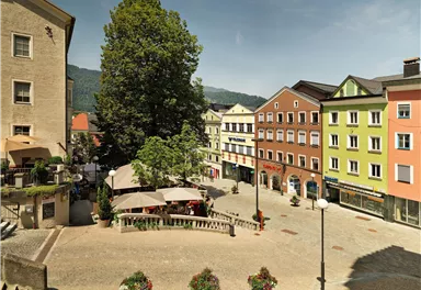 A vibrant city view with colorful buildings and a large tree. Outdoor tables invite you to linger.