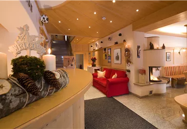 Ein einladender Empfangsbereich mit einem roten Sofa und einem Kamin. Die warmen Holzverkleidungen und die gemütliche Beleuchtung schaffen eine angenehme Atmosphäre.