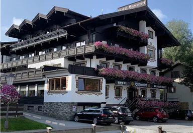 Ein charmantes Hotel im traditionellen alpinen Stil mit blühenden Balkonpflanzen. Die Fassade ist in Schwarz und Weiß gehalten und vermittelt eine einladende Atmosphäre.