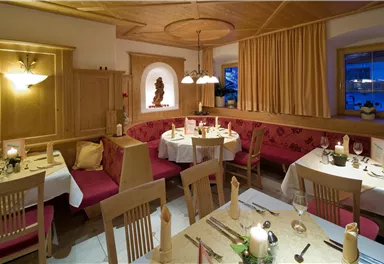 Ein gemütliches Restaurant mit Holzmöbeln und rot gepolsterten Bänken. Die Tische sind elegant gedeckt und Kerzen sorgen für eine warme Atmosphäre.