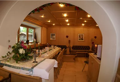 Ein gemütlicher Raum mit Holzwänden und einer festlich gedeckten Tafel. Die Atmosphäre ist einladend und warm.