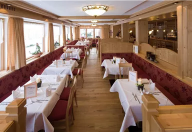 Ein gemütliches Restaurant mit Holzverkleidung und weißen Tischdecken. Es gibt viele Tische, die ordentlich mit Besteck und Blumen dekoriert sind.