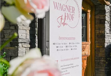 A sign of the Wagner Courtyard with opening hours and information. In the foreground, delicate pink roses can be seen.