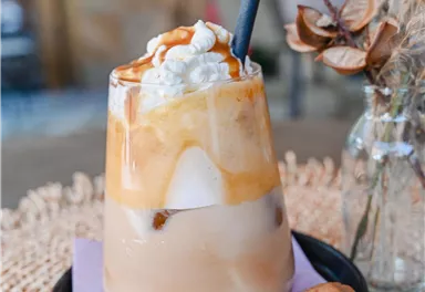 A delicious cold drink with cream and caramel over ice. A cookie is placed on a black plate.