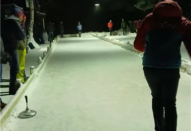 A snowy ice rink at night with illuminated areas. Some people are actively playing.