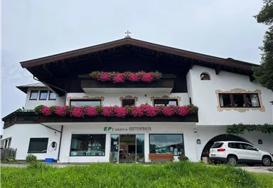 Ein charmantes Haus mit traditoneller Architektur, geschmückt mit bunten Blumen. Im Vordergrund parkt ein Auto, umgeben von einer grünen Wiese.