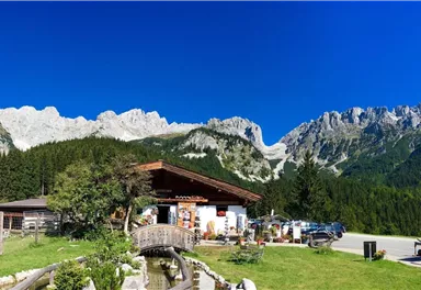 Ein gemütliches Gebäude in den Bergen mit einer schönen Landschaft. Im Hintergrund sind majestätische Berge und ein klarer blauer Himmel zu sehen.