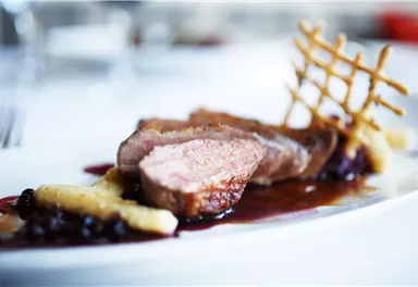 A delicate dish with juicy meat, garnished with fruit and a red sauce. Decorative accompaniments complete the appealing presentation.