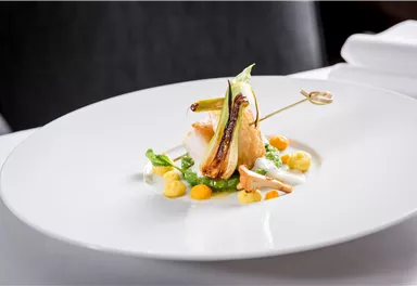 An artistically arranged dish on a white plate. It contains fish, vegetables, and colorful sauces as garnish.