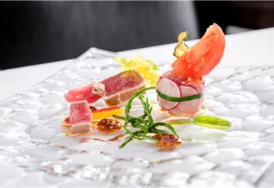 An elegant dish with freshly prepared fish, shrimp, and vegetables. It is artfully arranged on a glass plate.