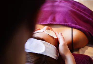 A person is receiving a facial treatment with eye pads. The environment is relaxing and friendly.