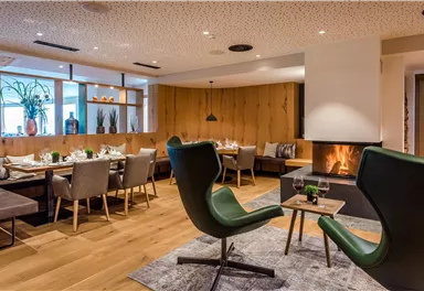 A modern restaurant with cozy seating areas and an open fireplace. The wooden paneling and soft lighting create an inviting atmosphere.