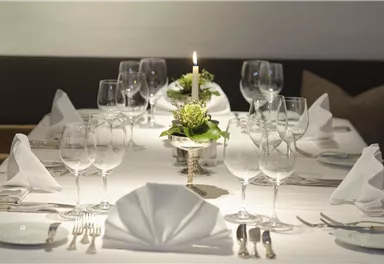 An elegantly set table with glasses, cutlery, and napkins. In the middle stands a candle with fresh flowers.