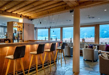 A modern bar with wooden decor and comfortable seating. Large windows offer a view of a picturesque landscape.