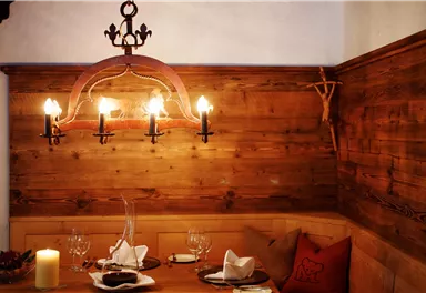 A cozy dining area with wooden walls and an elegant chandelier. On the table are white napkins, glasses, and a candle holder.