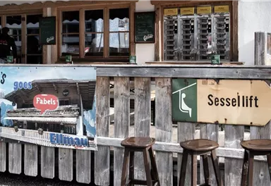 Eine rustikale Berghütte mit Holzbar und einem Schild zum Sessellift. Im Hintergrund sind Getränke und eine einladende Atmosphäre zu sehen.