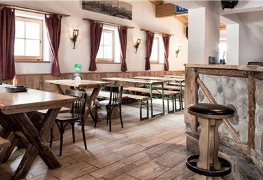 Ein gemütliches Restaurant mit Holztischen und Bänken. Die Atmosphäre ist einladend, mit roten Vorhängen und warmem Licht.