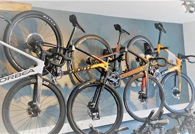 Drei Fahrräder der Marke Orbea hängen an einer Wand. Sie sind in verschiedenen Farben und Designs ausgeführt.