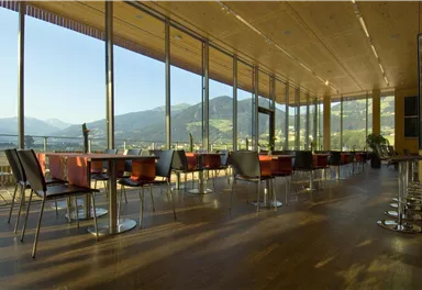A modern restaurant with large windows and a view of the mountains. The decor is minimalist and inviting.