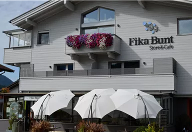 A charming café named "Fika Bunt" in a modern building. In the foreground are shade-providing sun umbrellas.