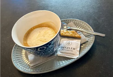 A cup of coffee with crema on an elegant plate. Next to it is a pastry and a sugar sweetener.