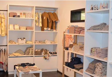 A cozy store with shelves full of baby clothes and accessories. The products are neatly displayed and in soft colors.