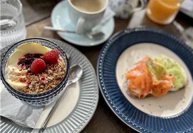 A set table with various breakfast dishes. In the foreground, a yogurt with berries and a snack made of salmon and vegetables.