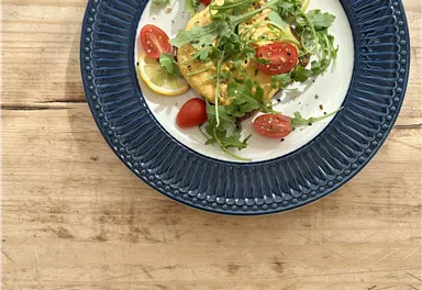 An appetizing plate with fried fish, garnished with fresh arugula, cherry tomatoes, and lemon slices. The plate is placed on a rustic wooden table.