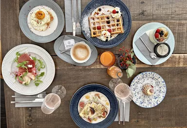 A beautifully set table with various dishes for breakfast. There are waffles, eggs, cold cuts, and drinks like coffee and juice.