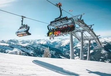 Eine Seilbahn transportiert Skifahrer über schneebedeckte Berge. Die Landschaft ist sonnig und klar, mit einem blauen Himmel.