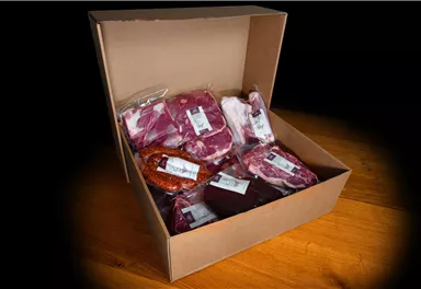 Eine offene Kartonbox mit verschiedenen Fleischpaketen. Die Verpackungen sind beschriftet und enthalten unterschiedliche Fleischsorten.